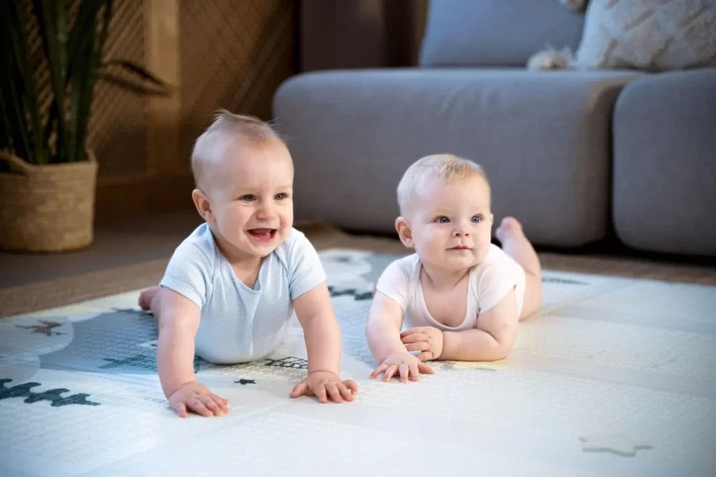 dua bayi berbaring di atas playmat bayi