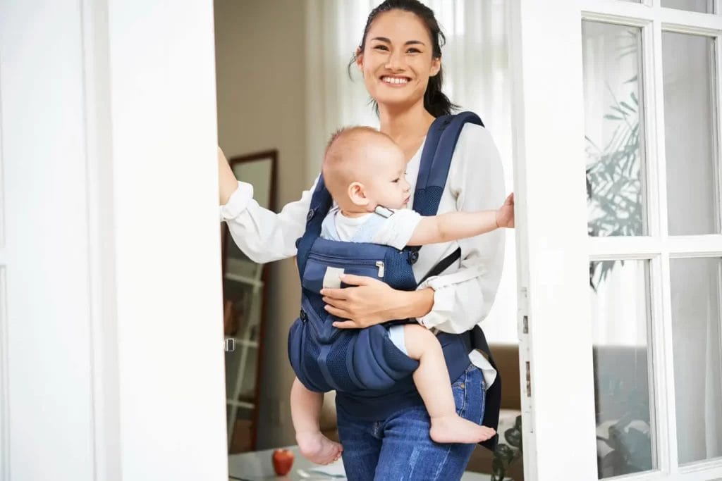 ibu tersenyum menggendong bayi dekat jendela