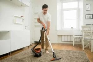 pria membersihkan karpet dengan vacuum cleaner