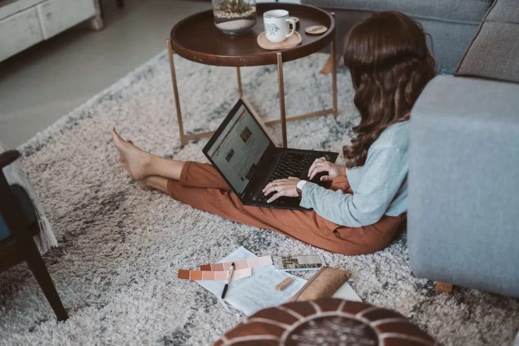 wanita buka laptop duduk di atas karpet