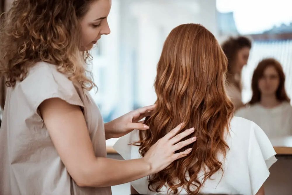 seorang perempuan sedang membenarkan rambut perempuan lain di dalam salon