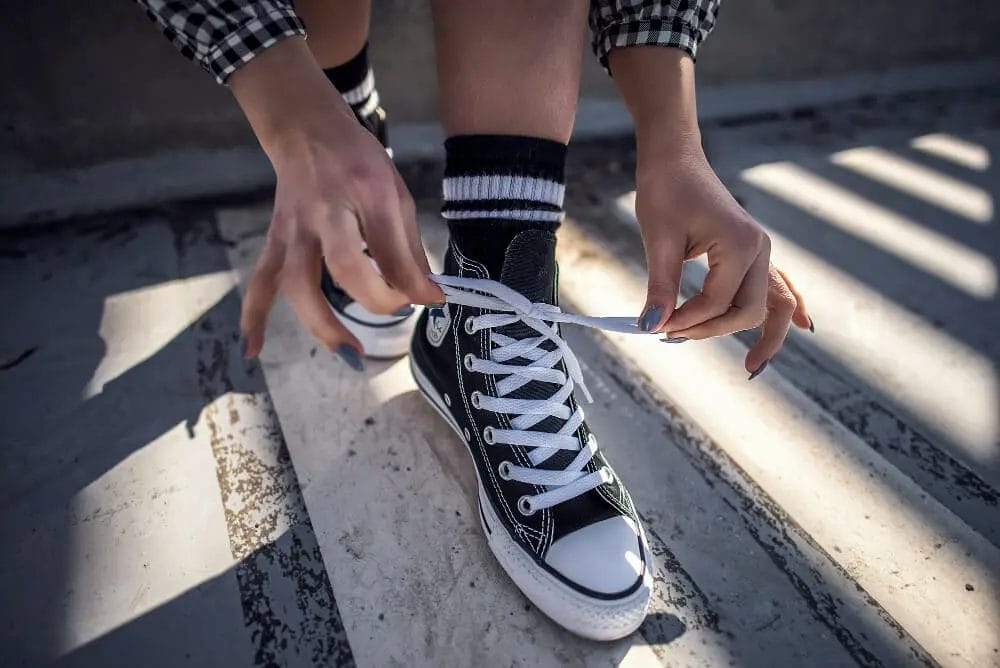 wanita membenarkan tali sepatu converse