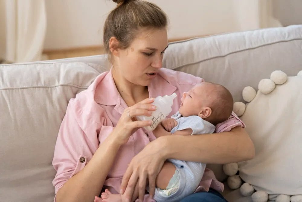 ibu berbaju pink memberikan susu botol ke bayi